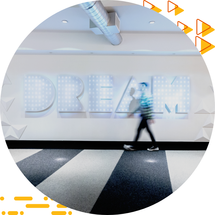 Large white wall with the word DREAM on it; in the foreground, a blurry outline of a male student walking past.